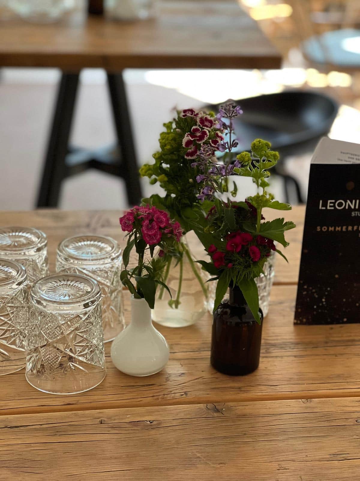 Tischdeko mit Bartnelken und Wiesenblumen in kleinen Vasen auf Holztisch