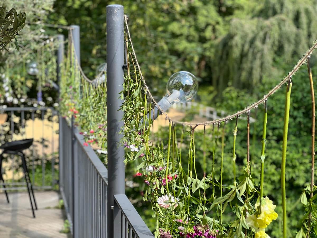 Blumengirlande mit Lichterkugeln am Gelaender einer Sommerterrasse