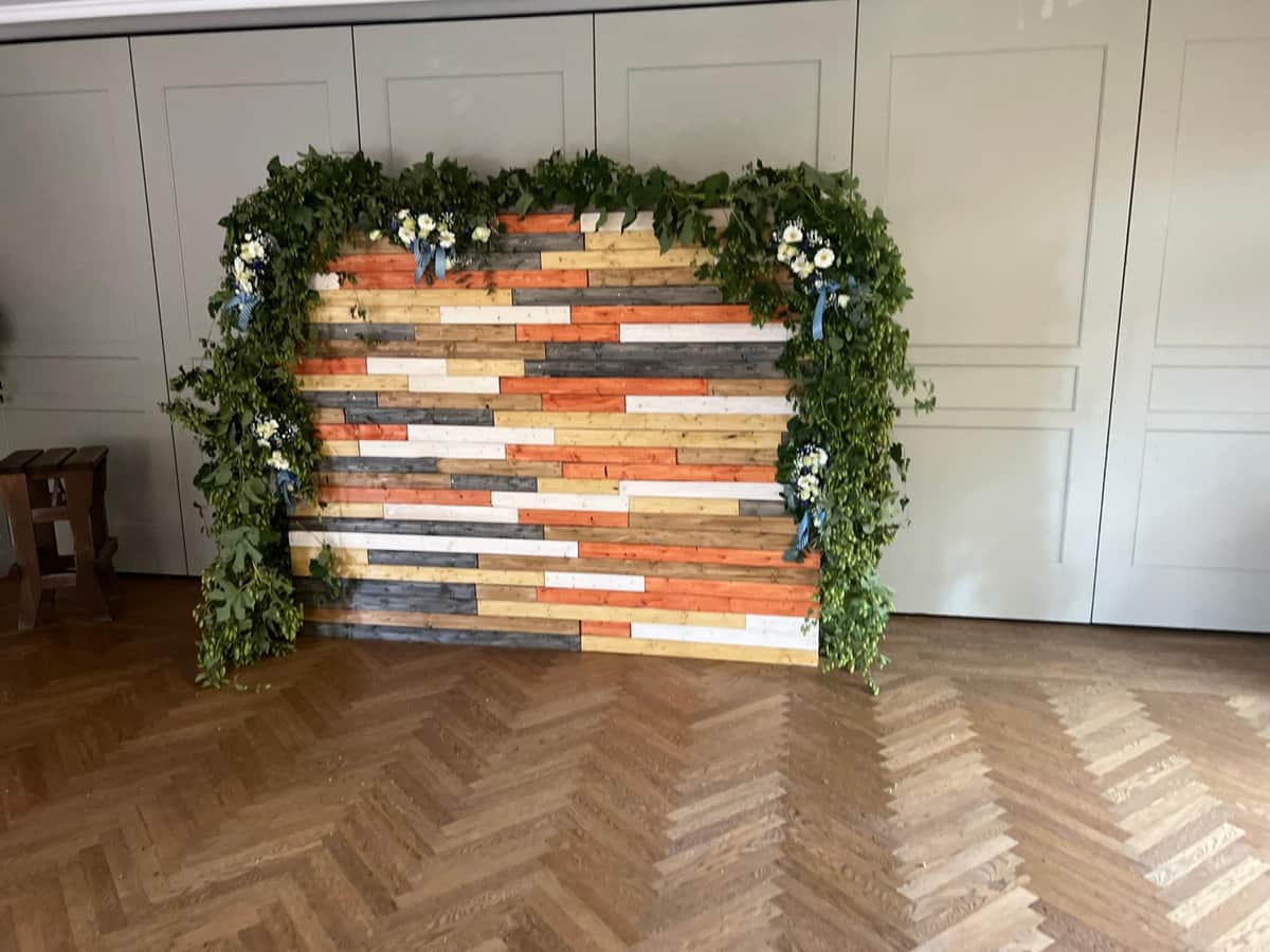 Fotowand aus bunten Holzlatten mit Eukalyptus-Girlande und Blumen
