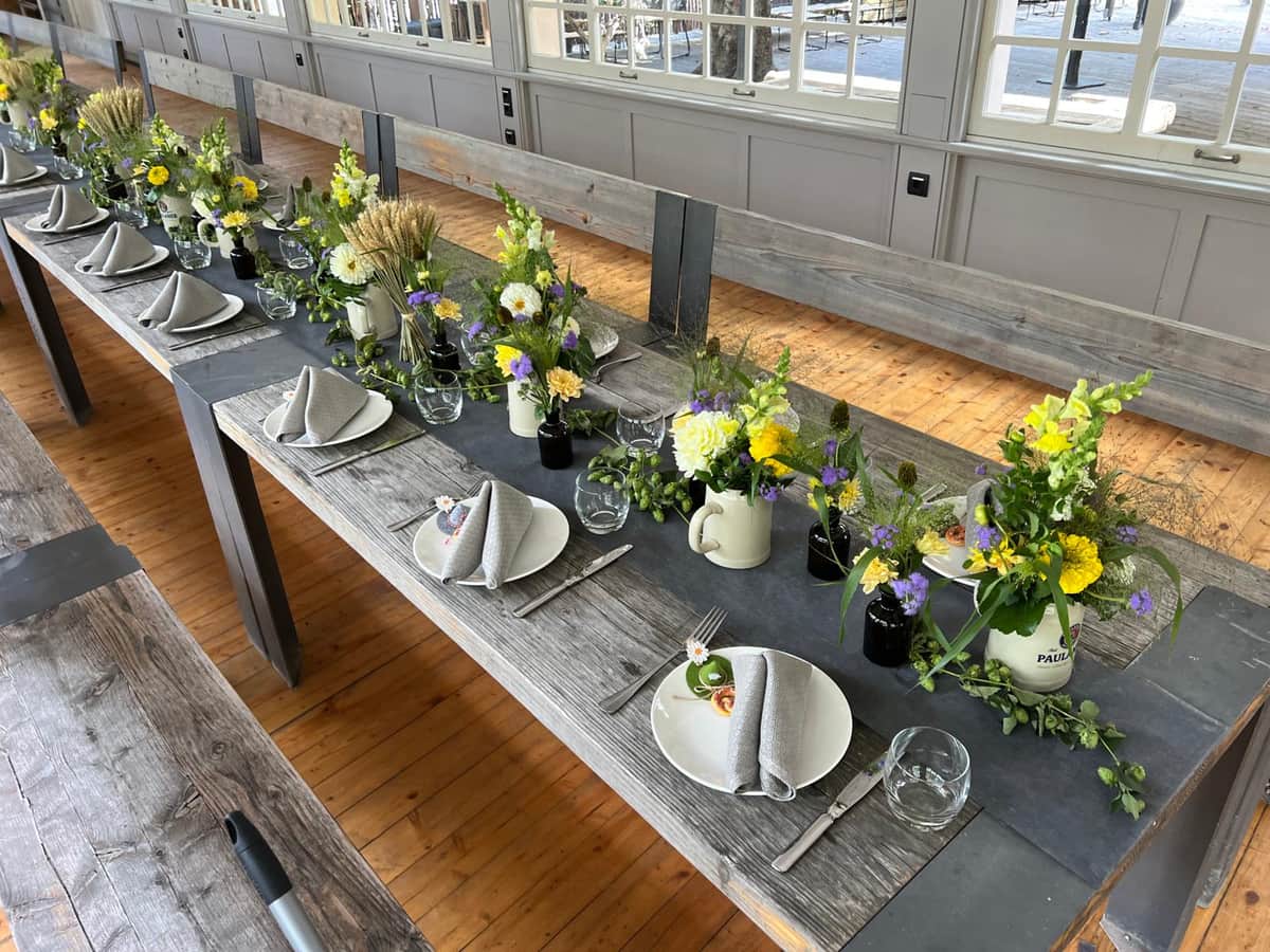 Rustikal gedeckte Festtafel mit Wiesenblumen in Bierkruegen