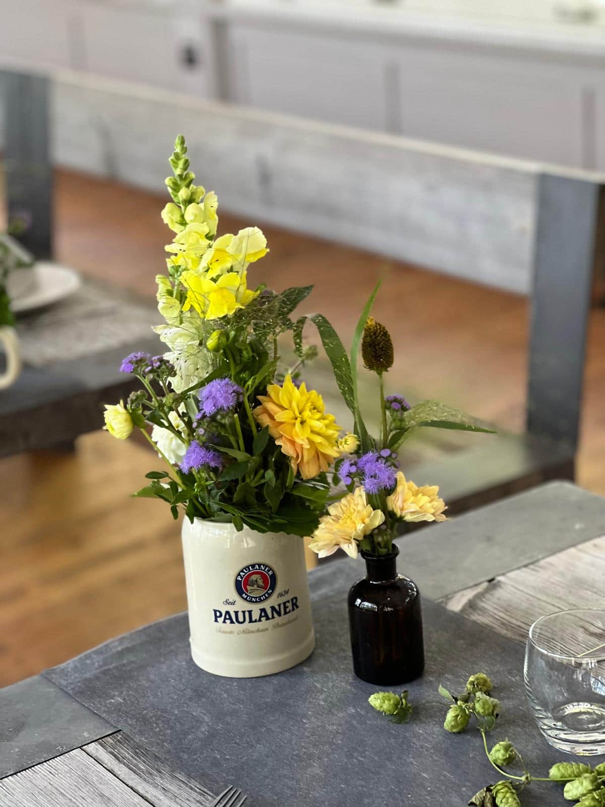 Blumenarrangement mit gelben Loewenmaeulchen und Dahlien im Bierkrug