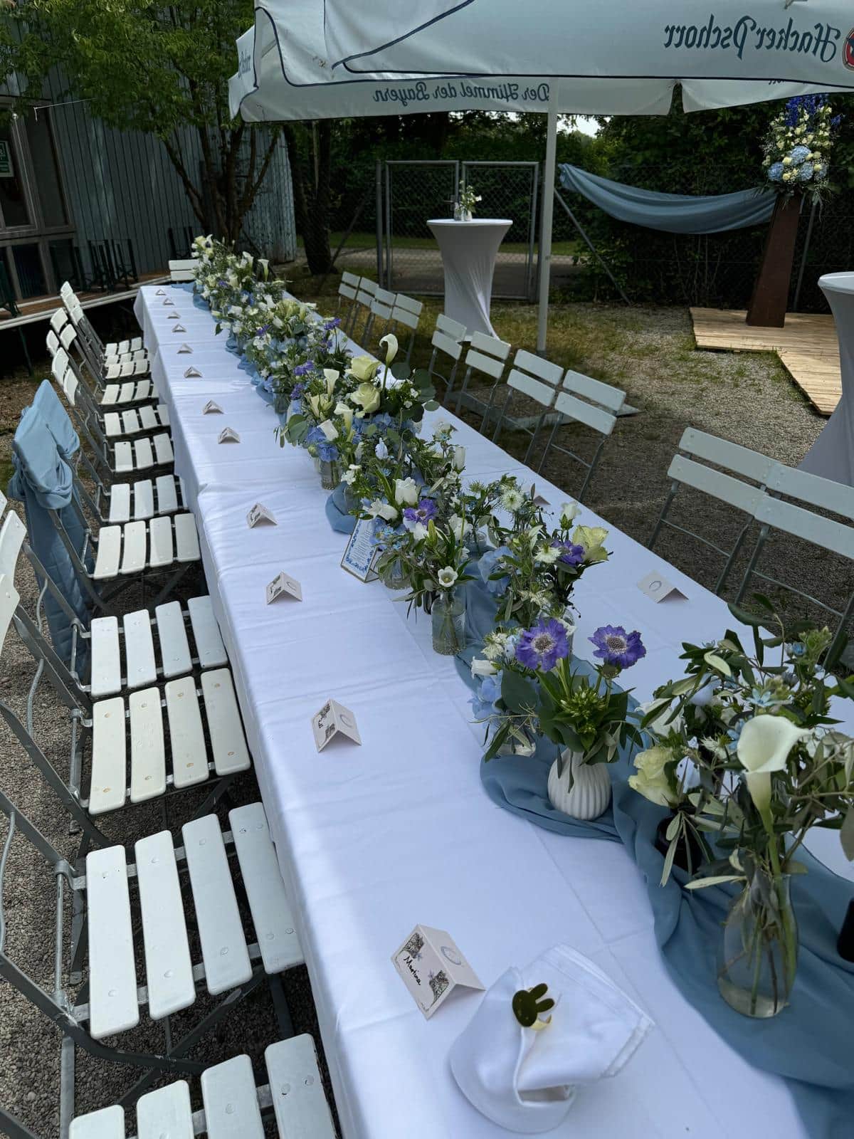 Sommerlich gedeckte Garten-Festtafel mit blau-weissen Blumenarrangements