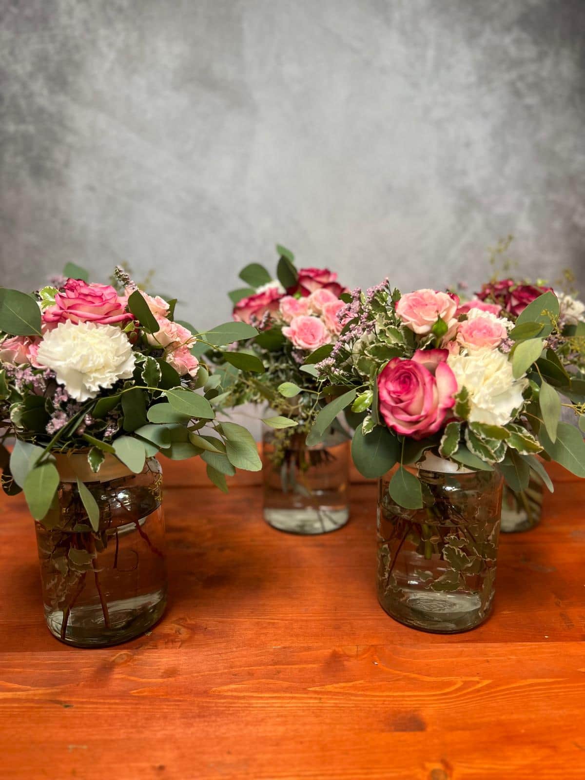 Drei Glasvasen mit rosa Rosen, Nelken und Eukalyptus als Tischdekoration