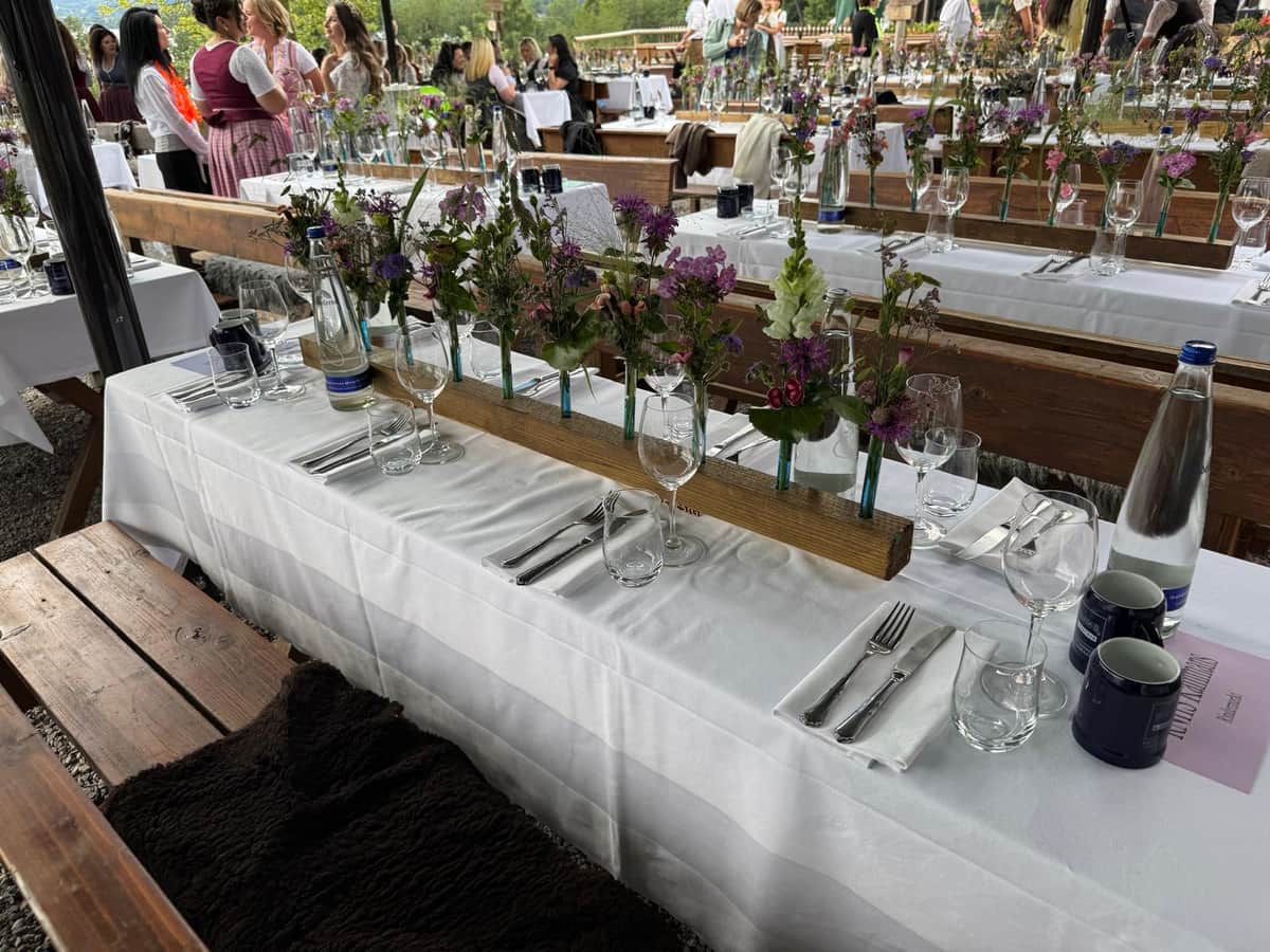 Bayerisches Biergarten-Event mit Gaesten und Tischdeko aus Wiesenblumen