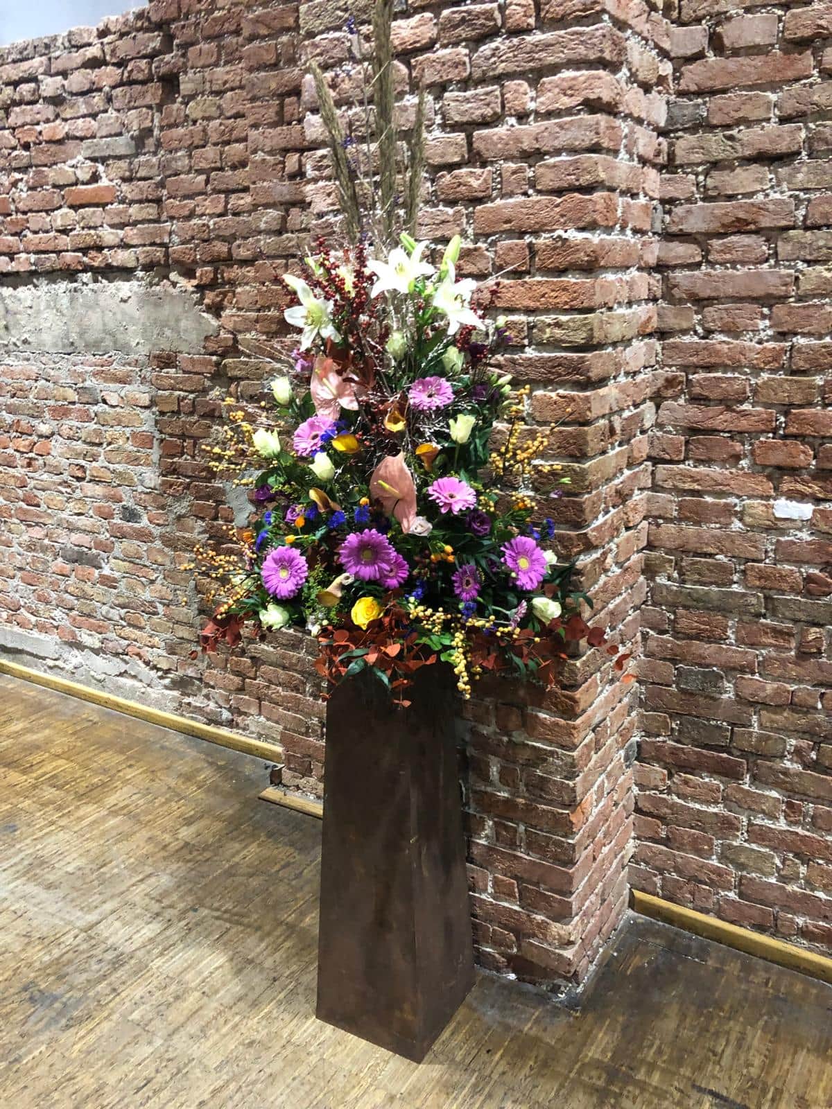 Farbenfroher Blumenstrauss mit Lilien und Chrysanthemen auf rostfarbenem Sockel