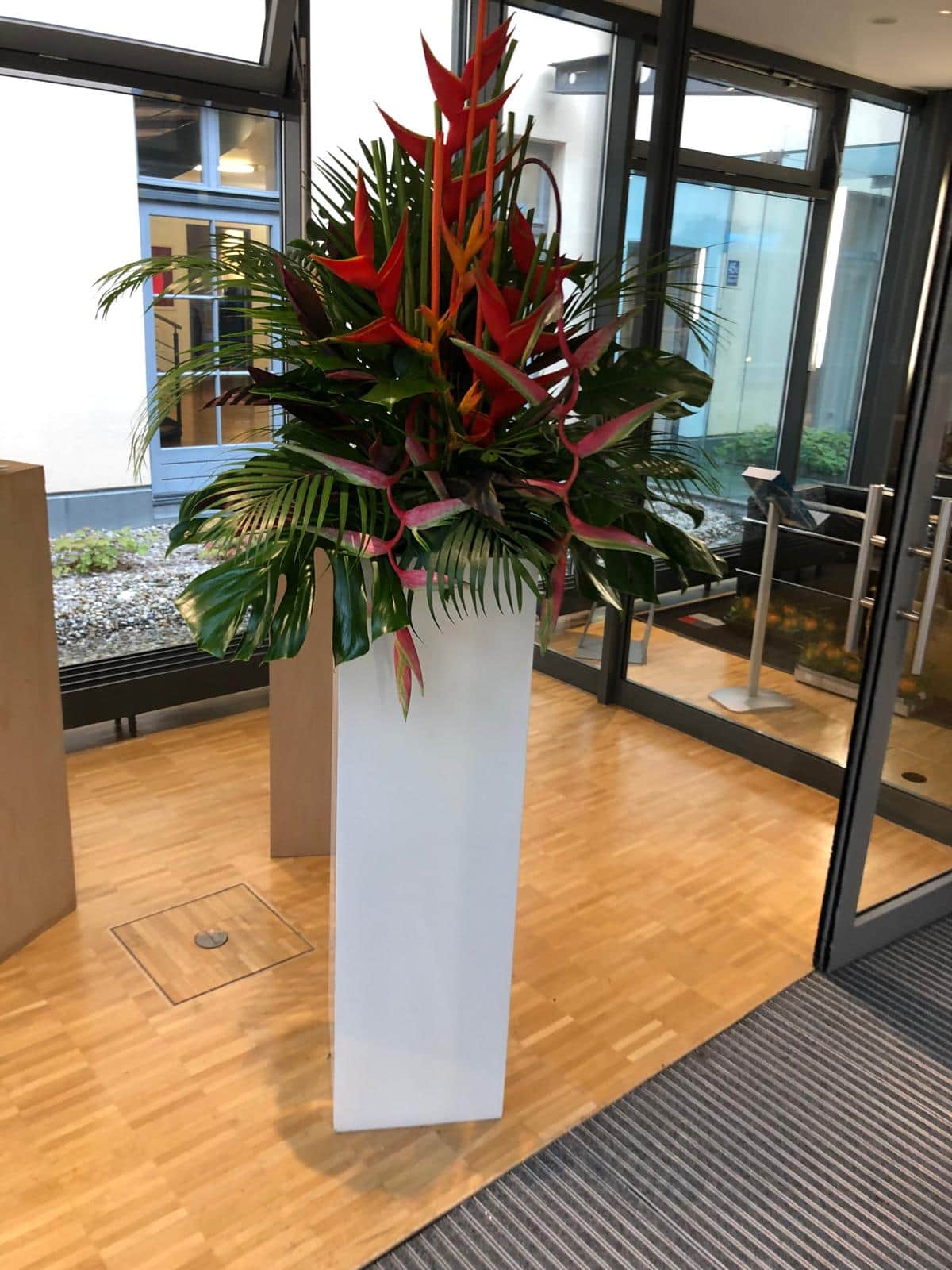 Hohe tropische Blumendekoration mit Helikonien auf weisser Saeule