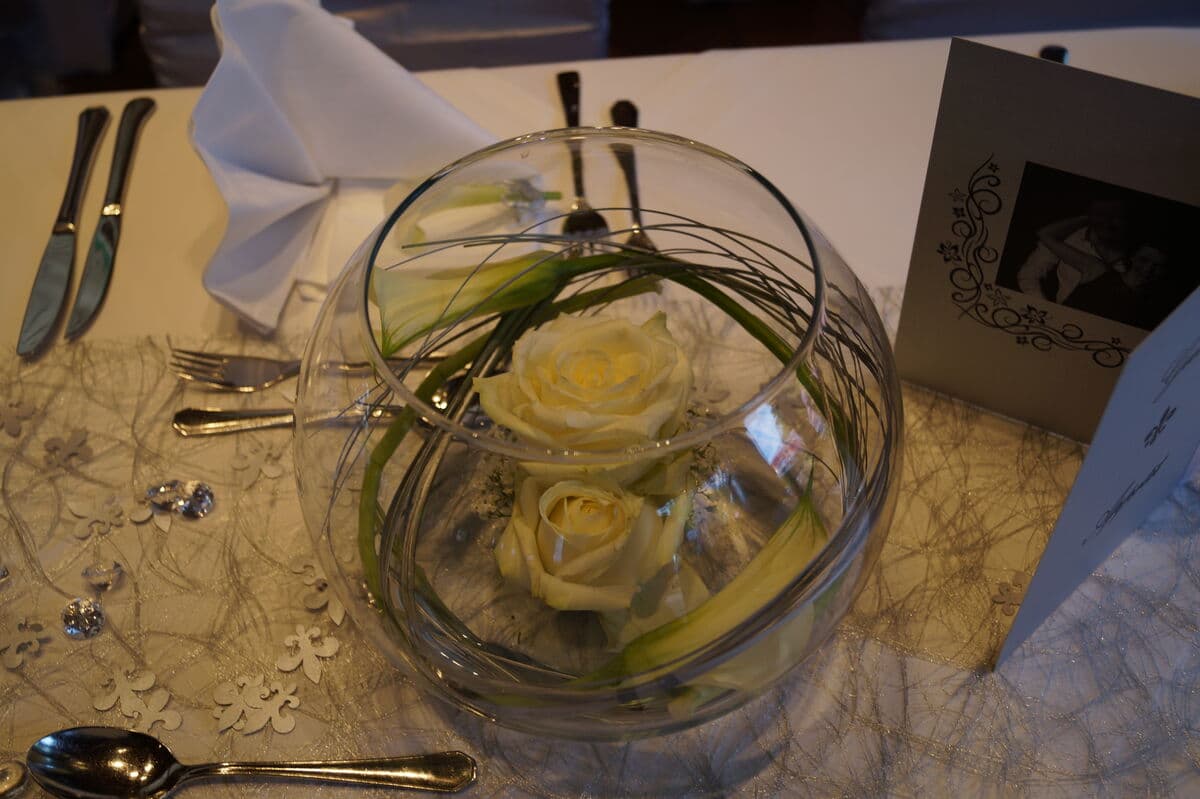 Tischdekoration mit weißen Rosen in Glaskugel und Platzkarte