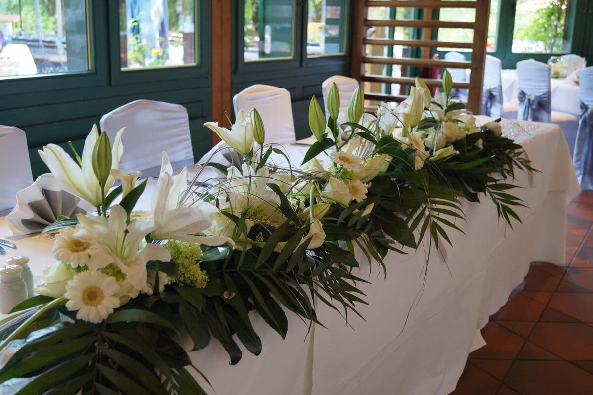 Brautpaartisch mit üppiger Blumengirlande aus weißen Lilien und Gerbera